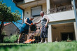 © qunica.com - Two men work together in a bright yard, guiding a lawn mower as they maintain the grass in front of a house, highlighting outdoor activity and teamwork on a sunny day.