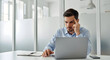 © Ali - European business man holding hand near temples, feeling stressed and tired sitting at office workplace. Focused upset young businessman looking at laptop pc computer screen having stress.