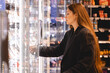 © zvkate - Woman in a supermarket standing in front of the freezer looking for her favorite frozen food. Woman opens the refrigerator door with a product in a supermarket. Girl chooses salmon in grocery store.