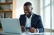 © Viktor - Young businessman uses laptop to make online payment with credit card. He smiles while completing a transaction via mobile banking app in an office setting. Modern digital commerce concept.