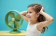 © Viktor - Smiling girl stands near a green fan. Kid enjoys cool air flow at hot summer indoors. She holds her hair up feeling refreshment from fan breeze. Concept of heat and relaxation.