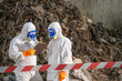 © BESTIMAGE - Two forensic investigators wea protective suits and masks examining evidence at a crime scene near a large pile of debris and dirt, safety tape in place