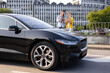 © sofiko14 - A man and woman discuss work while standing near a sleek black electric car in an urban setting.