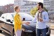 © sofiko14 - A man and a woman shake hands near a sleek black electric car, possibly after a business deal or meeting.