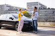 © sofiko14 - Two friends celebrate with a high-five next to a sleek black electric car in an urban setting, possibly after a successful ride.