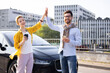 © sofiko14 - Two friends celebrate with a high-five next to a car, one holding a coffee cup and the other a phone.