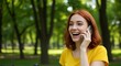 © Devan - Woman smiling while using mobile phone in a park setting