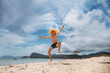 © Aboltin - Happy young man leaping on sandy beach with big smile, arms raised in excitement. Clear sky, mountains and sea in background capture essence of beach vacation freedom.