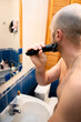 © dizfoto1973 - A bald man uses an electric trimmer to shave his beard in a bright bathroom, focusing on his reflection. Capturing a daily grooming routine, self-care, and hygiene.