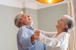© Daniel - Joyful active old retired romantic couple dancing laughing in living room, happy middle aged wife and elder husband having fun at home, smiling senior family grandparents relaxing bonding together