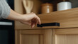 © photo for everything - A hand gently reaches for a sleek, modern black handle on a light-toned wooden kitchen cabinet, hinting at the preparation of a meal or accessing kitchen essentials.