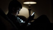 © photo for everything - A young boy sits in a dimly lit room, illuminated by the glow of his smartphone. Engaged in its digital world, he scrolls, taps, and immerses himself in virtual entertainment.