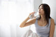 © hidez - Young Woman Drinking Water on Bed in Bright Minimal Bedroom