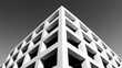 © Asad - A captivating black and white photograph captures the corner of a modern building with a geometric facade, showcasing a pattern of square openings against a clear sky, emphasizing architectural design