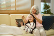 © Stella 16 - Smiling granddaughter and grandmother with tablet pc computer sitting on couch at home.