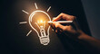 © Sharif Studio - A hand draws a glowing light bulb with chalk on a dark blackboard. Concept of idea, inspiration, and innovation. Bright light emanating from filament, symbolizing creative thought and problem-solving.