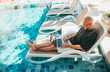 © Soloviova Liudmyla - Bald middle aged freelancer business owner working laptop on sun lounger by luxury hotel swimming pool. Digital nomad successfully managing company remote tropical vacation sunlit summer day.