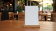 © alinea - Blank acrylic menu stand mockup on a wooden café table with warm blurred background. Ideal for showcasing restaurant menus, promotions, or food and drink advertising designs.