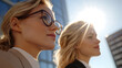 © photo for everything - Two confident businesswomen gaze towards the horizon, standing against the backdrop of a modern office building bathed in the sunlight, symbolizing ambition and achievement.