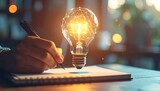 Main écrivant dans un cahier à côté d'une ampoule lumineuse avec un filament géométrique, symbolisant l'idée, l'innovation et la créativité