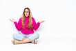 © luismolinero - Young caucasian woman sitting on the floor isolated on white background having doubts while raising hands