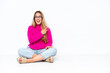 © luismolinero - Young caucasian woman sitting on the floor isolated on white background surprised and pointing side