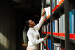 © Drobot Dean - A female student is standing and smiling while taking out a book from a bookshelf