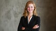© Formoney - A young woman stands in a modern office setting with a confident smile wearing a black suit. Her arms are crossed and the gray wall creates a stylish background.