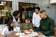 © Drobot Dean - A group of five workers are talking and looking at documents on a table with three of them sitting while two of them stand