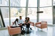 © Drobot Dean - A group of three workers are looking at a laptop on a table while talking and sitting on a sofa and a chair
