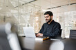 © muse studio - Man working on laptop in a modern office setting with glass walls and minimalistic design