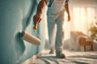 © whitestorm - A painter applying fresh light blue paint to a room wall with a roller.