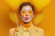 © Jon Stock - Bright yellow fashion portrait featuring a model with yellow balloons and sunglasses, set against a vibrant yellow background in a studio