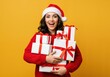 © Vasiliy - Happy young woman in a Santa hat holding a stack of Christmas gifts. Excited smiling girl with presents on a yellow background. Holiday celebration concept with copy space
