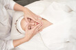 © elenavolf - Young caucasian female receiving relaxing facial massage at spa in white robe.