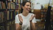 © Krakenimages.com - Woman clapping hands and smiling in a library building among bookshelves and aisles; joy celebration enthusiasm.