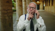 © Krakenimages.com - Senior man in business suit makes a silence gesture while speaking on a phone in an old university hallway.