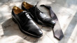 © Farid - A pair of polished black leather business shoes and silk tie placed on marble floor under daylight.