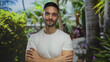 © Krakenimages.com - Young hispanic man smiling in a lush green park outdoors wearing a white shirt showcasing natural beauty and relaxation among vibrant plants and peaceful atmosphere.