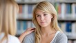 © OlgaKhorkova - A young blonde woman with a thoughtful expression is engaged in a conversation in a library setting. Another person, seen from the back, has a comforting hand on her shoulder. The focus is on the youn