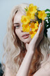 © VICHIZH - Beautiful model with long wavy blonde hair holding vibrant yellow flowers, showcasing a fresh and airy aesthetic in a spring-inspired setting.