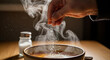 © kelum - Close-up shot of a hand sprinkling salt over a steaming bowl of food on a wooden table.