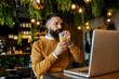 © Dusan Petkovic - Portrait of thirsty smart casual freelancer sitting in coffee shop and drinking fresh orange juice from coffee shop while looking at the laptop.