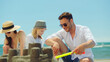 © Videophilia - Happy family, mother, father, and daughter, enjoying their summer vacation by building a sandcastle together on a sunny beach, sharing moments of leisure and childhood joy under a clear blue sky