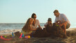 © Videophilia - Happy family of four enjoying summer beach vacation, parents with two young children building a sandcastle on the sand by the ocean at sunset, fostering togetherness and fun