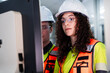 © KANGWANS - A woman wearing a yellow and orange safety vest is looking at a computer monitor
