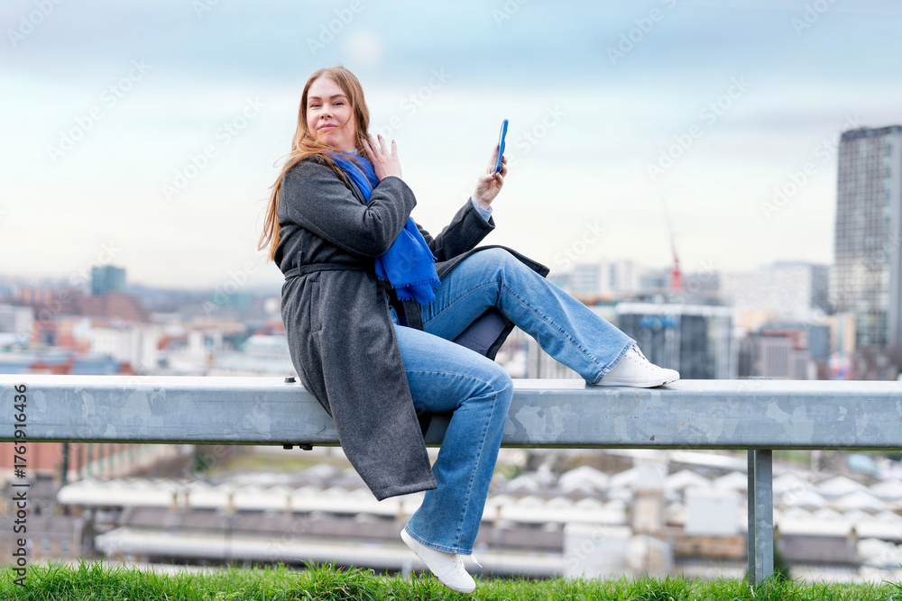 Someone Sitting Railing Young woman enjoying city views while sitting on a railing with a ...