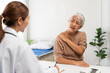 © amnaj - Senior woman suffering from shoulder pain seeing a doctor for examination, diagnosis, and treatment in a clinic