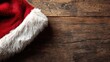 © Aleeza - Close up of a fluffy red santa hat with white trim resting on a rustic wooden surface