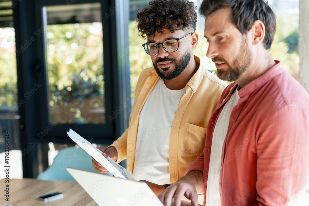 Diverse business team collaborating on project using laptop Stock Photo ...